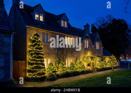 Weihnachtslichter auf einem cotswold Cottage in Lower Slaughter in der Abenddämmerung im Dezember. Lower Slaughter, Cotswolds, Gloucestershire, England Stockfoto