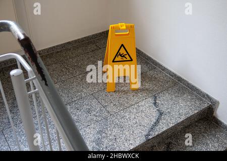 Ein gelbes Schild warnt vor einem Verrutschen im Treppenhaus Stockfoto