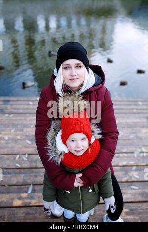 Junge Mutter zu Fuß mit ihrem niedlichen kleinen Tochter draußen in Stadtpark in der Nähe des Flusses Stockfoto