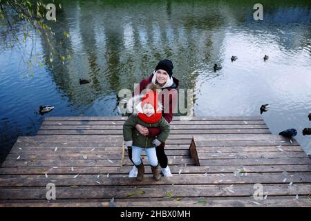 Junge Mutter zu Fuß mit ihrem niedlichen kleinen Tochter draußen in Stadtpark in der Nähe des Flusses Stockfoto