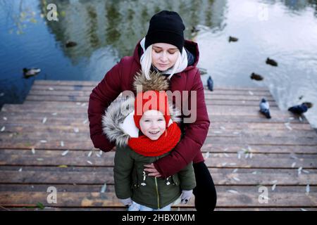 Junge Mutter zu Fuß mit ihrem niedlichen kleinen Tochter draußen in Stadtpark in der Nähe des Flusses Stockfoto