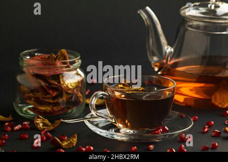 Kräutertee aus hausgemachtem Granatapfel in Teekannen aus Glas und Tasse auf schwarzer Oberfläche mit Granatapfel aus trockener Schale Stockfoto
