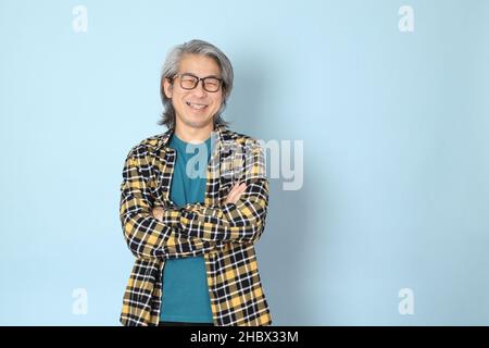 Der ältere asiatische Mann mit gelbem karierten Hemd, das auf dem blauen Hintergrund steht. Stockfoto