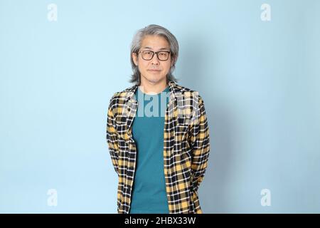 Der ältere asiatische Mann mit gelbem karierten Hemd, das auf dem blauen Hintergrund steht. Stockfoto