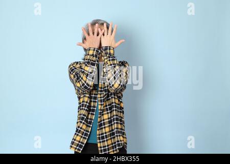 Der ältere asiatische Mann mit gelbem karierten Hemd, das auf dem blauen Hintergrund steht. Stockfoto