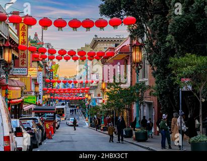 San Francisco, USA - 18. Dezember 2021: Traditionelle Geschäfte, Laternen und Menschen auf der Straße in Chinatown in der Nähe der Innenstadt mit einem feurigen Sonnenuntergang Stockfoto