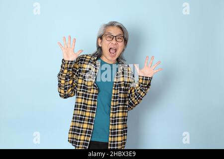 Der ältere asiatische Mann mit gelbem karierten Hemd, das auf dem blauen Hintergrund steht. Stockfoto