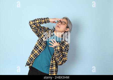 Der ältere asiatische Mann mit gelbem karierten Hemd, das auf dem blauen Hintergrund steht. Stockfoto