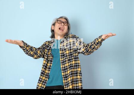 Der ältere asiatische Mann mit gelbem karierten Hemd, das auf dem blauen Hintergrund steht. Stockfoto