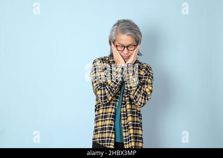 Der ältere asiatische Mann mit gelbem karierten Hemd, das auf dem blauen Hintergrund steht. Stockfoto