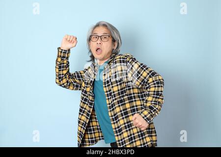 Der ältere asiatische Mann mit gelbem karierten Hemd, das auf dem blauen Hintergrund steht. Stockfoto