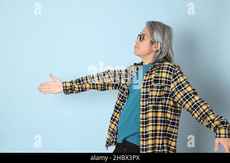 Der ältere asiatische Mann mit gelbem karierten Hemd, das auf dem blauen Hintergrund steht. Stockfoto