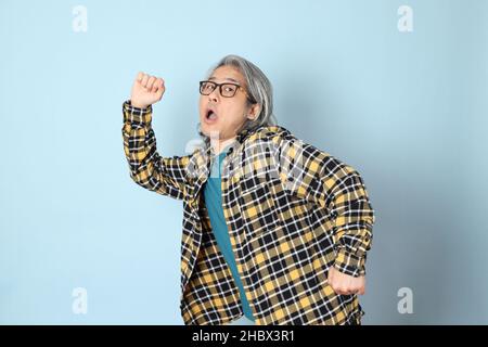 Der ältere asiatische Mann mit gelbem karierten Hemd, das auf dem blauen Hintergrund steht. Stockfoto