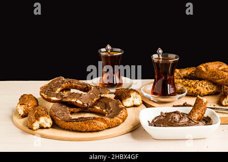 Traditioneller türkischer knuspriger Bagel, mit Cremeschokolade auf dem Holzteller mit Messer und Tee köcheln lassen. Stockfoto