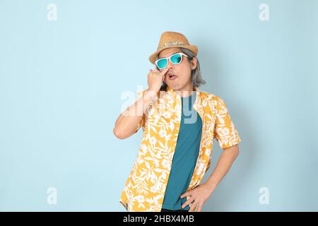 Der ältere asiatische Mann trägt Sommer gekleidet stehen auf dem blauen Hintergrund. Stockfoto