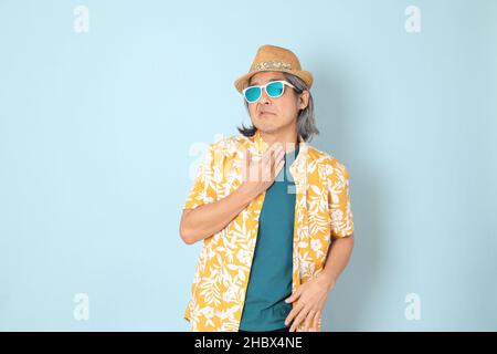 Der ältere asiatische Mann trägt Sommer gekleidet stehen auf dem blauen Hintergrund. Stockfoto