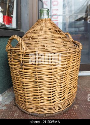 Vintage Weinflaschen im Korbkorb auf einem Fass. Alte leere Weidenweinflasche. Stockfoto