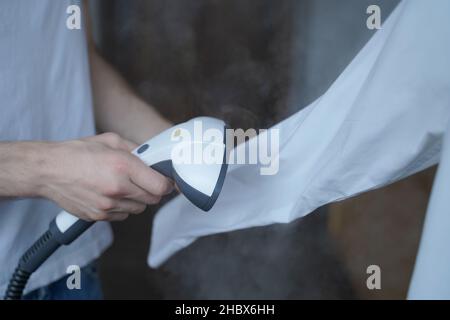 Beschnittenes Foto eines Mannes mit Dampfgarer, der das weiße Hemd ordentlich bügelt und dabei lange Ärmel hält Stockfoto