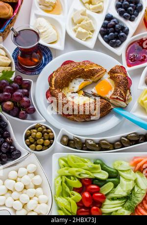 Traditionelles türkisches Frühstück mit türkischem Bagel, Simit, Oliven und Tee. Ein Stück mit blauem Messer geschnitten, oben. Stockfoto