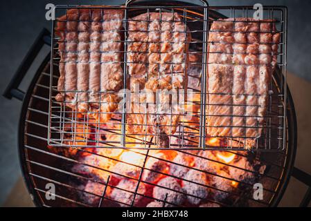 Grilldetails mit frischem Lachs, der von oben betrachtet auf brennenden heißen Kohlenstoffen gegrillt oder geröstet wird. BBQ Schmelzen von Fisch in einem Grill auf Live-Feuer Stockfoto