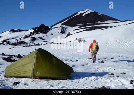 Winterbasislager am Vulkankrater im Ätna Park, Wanderer mit Rucksack zieht sich vom Zelt weg [1b] Stockfoto