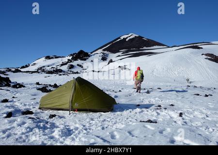 Winterbasislager am Vulkankrater im Ätna Park, Wanderer mit Rucksack zieht sich vom Zelt weg [1b] Stockfoto