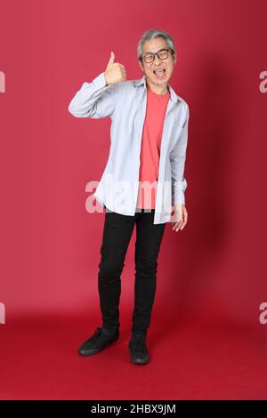 Der ältere asiatische Mann trägt ein blaues Hemd mit langen Haaren, die auf dem roten Hintergrund stehen. Stockfoto