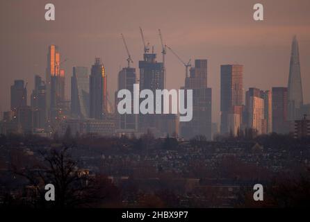 London, Großbritannien. 22. Dezember 2021. Wechselnde Lichtverhältnisse auf Londoner Wolkenkratzern während eines farbenfrohen Wintersonnenaufgangs, bei dem Sonnenlicht die oberen Stockwerke der höchsten Bürogebäude trifft. Aufsteigendes Sonnenlicht trifft den Gipfel des Bishopsgate aus dem Jahr 22 (links im Bild), dem höchsten Gebäude der City of London. Die Sanierung von Hochhäusern in Vauxhall (in der Mitte) verdeckt allmählich einige der Bürogebäude der Stadt, die von Wimbledon aus gesehen werden. Quelle: Malcolm Park/Alamy Live News Stockfoto