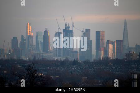 London, Großbritannien. 22. Dezember 2021. Wechselnde Lichtverhältnisse auf Londoner Wolkenkratzern während eines farbenfrohen Wintersonnenaufgangs, bei dem Sonnenlicht die oberen Stockwerke der höchsten Bürogebäude trifft. Aufsteigendes Sonnenlicht trifft den Gipfel des Bishopsgate aus dem Jahr 22 (links im Bild), dem höchsten Gebäude der City of London. Die Sanierung von Hochhäusern in Vauxhall (in der Mitte) verdeckt allmählich einige der Bürogebäude der Stadt, die von Wimbledon aus gesehen werden. Quelle: Malcolm Park/Alamy Live News Stockfoto