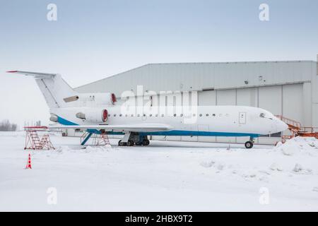 Weißes Passagierflugzeug in der Nähe des Flugzeughangars bei kaltem Winterwetter Stockfoto