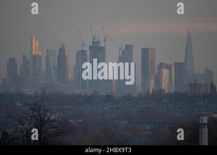 London, Großbritannien. 22. Dezember 2021. Wechselnde Lichtverhältnisse auf Londoner Wolkenkratzern während eines farbenfrohen Wintersonnenaufgangs, bei dem Sonnenlicht die oberen Stockwerke der höchsten Bürogebäude trifft. Aufsteigendes Sonnenlicht trifft den Gipfel des Bishopsgate aus dem Jahr 22 (links im Bild), dem höchsten Gebäude der City of London. Die Sanierung von Hochhäusern in Vauxhall (in der Mitte) verdeckt allmählich einige der Bürogebäude der Stadt, die von Wimbledon aus gesehen werden. Quelle: Malcolm Park/Alamy Live News Stockfoto