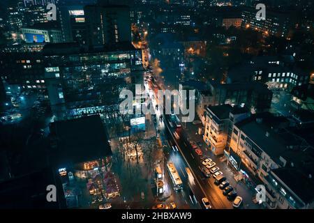 Nachtverkehr in der Stadt zwischen Stadtgebäuden und Neonlichtern. Verkehr auf Nezalezhnosti Avenue in der Nähe des Hotels Kharkiv in der Nacht: Luftdrohnenansicht: 21. Dezember 2021 - Kharkiv, Ukraine. Stockfoto