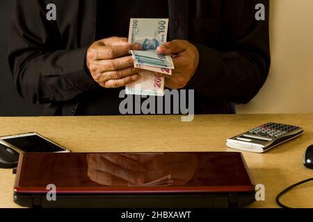 Die Hand eines Mannes in schwarzem Hemd zählt sein Geld türkische Banknoten an seinem Schreibtisch. Stockfoto