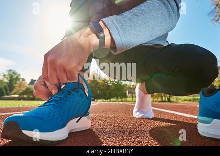 Männlicher Läufer in blauen Sneakers mach dich bereit für den Lauf auf der Stadionstrecke, aus nächster Nähe. Männliche Hände binden an Sport-Sneakers zum Joggen. Fitness und gesundes Lifestyle-Konzept Stockfoto