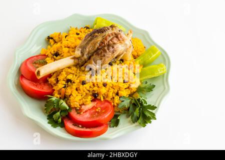 Traditioneller arabischer Reis, Pilaff mit Tomate, Pfeffer, Petersilie und Lammschenkel in Teller auf weißer Oberfläche. Opferfest Konzept Stockfoto