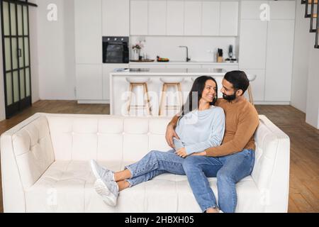 Sanftes und liebliches verliebter Paare, die auf dem bequemen Sofa zu Hause umarmt sitzen und sich zärtlich zuschauen. Konzept der Unterstützung und Fürsorge in der Ehe Stockfoto