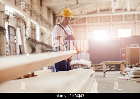 Seriöse männliche Baumeister trägt Holzbrett auf der Baustelle Stockfoto