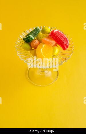 Bunte Süßigkeiten und Pralinen auf gelbem Hintergrund mit footed, Glas Candy Bowl.The Sugar Feast oder jede Feier Konzept entworfen. Stockfoto
