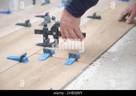 Mason Hände Anpassung Fliesenwader zwischen Keramik-Holz-Effekt Fliesen. Stockfoto