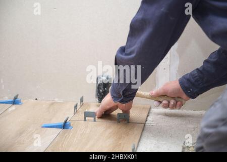 Hände von Senior Fliese Verlegung keramischen Holz-Effekt Fliesen mit einem Holzhammer. Stockfoto