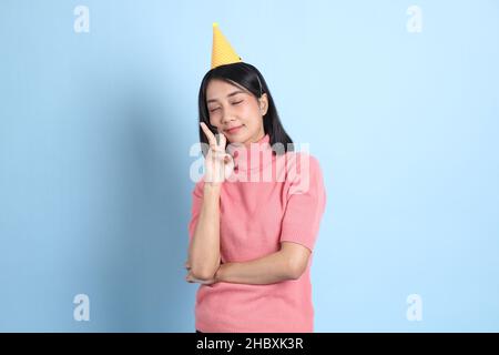 Die junge asiatische Frau trägt rosa Kleider und steht auf dem blauen Hintergrund. Stockfoto