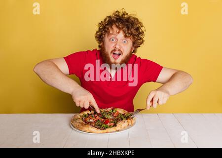 Porträt eines rotbärtigen Mannes, der sich bereit gemacht hat, leckere italienische Pizza zu essen, isoliert auf gelbem Studiohintergrund. Stockfoto