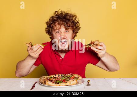 Porträt eines rotbärtigen Mannes, der sich bereit gemacht hat, leckere italienische Pizza zu essen, isoliert auf gelbem Studiohintergrund. Stockfoto