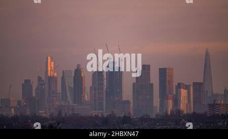 London, Großbritannien. 22. Dezember 2021. Wechselnde Lichtverhältnisse auf Londoner Wolkenkratzern während eines farbenfrohen Wintersonnenaufgangs, bei dem Sonnenlicht die oberen Stockwerke der höchsten Bürogebäude trifft. Aufsteigendes Sonnenlicht trifft auf die Spitze von 22 Bishopsgate (3rd links im Bild), dem höchsten Gebäude in der City of London. Die Entwicklung von Hochhauswohnungen in Vauxhall (Mitte im Bild mit Baukräne) verdeckt allmählich einige der Bürogebäude der Stadt in der „Square Mile“ von Wimbledon aus gesehen. Kredit: Malcolm Park/Alamy Stockfoto