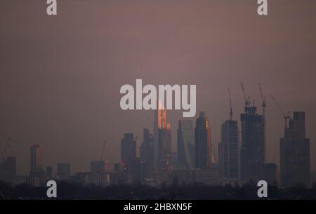 London, Großbritannien. 22. Dezember 2021. Wechselnde Lichtverhältnisse auf Londoner Wolkenkratzern während eines farbenfrohen Wintersonnenaufgangs, bei dem Sonnenlicht die oberen Stockwerke der höchsten Bürogebäude trifft. Aufsteigendes Sonnenlicht trifft auf die Spitze von 22 Bishopsgate (3rd links im Bild), dem höchsten Gebäude in der City of London. Die Entwicklung von Hochhauswohnungen in Vauxhall (Mitte im Bild mit Baukräne) verdeckt allmählich einige der Bürogebäude der Stadt in der „Square Mile“ von Wimbledon aus gesehen. Kredit: Malcolm Park/Alamy Stockfoto