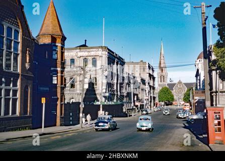 Ein Blick auf die Innenstadt von Christchurch, South Island, Neuseeland in c.. 1958. Am Ende der Straße befindet sich die Kathedrale von Christchurch. Aufgrund der Schäden und des Verlusts von Gebäuden, die durch Erdbeben verursacht wurden, vor allem durch das Erdbeben vom Februar 2011, sieht dieser Bereich nun völlig anders aus. Dies zerstörte den Turm und den größten Teil des Turms und beschädigte den Rest des Gebäudes schwer. Der Turm wurde anschließend abgerissen. Es wurde beschlossen, dass die Christchurch Cathedral wieder eingesetzt wird. Mitte 2019 hatten frühe Entwurfs- und Stabilisierungsarbeiten begonnen – ein Vintage-Foto aus dem Jahr 1950s. Stockfoto