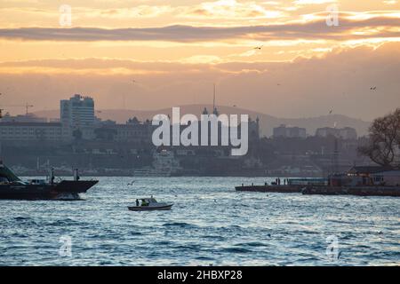Fischer in Fischerbooten und Linienfähren im Bosporus bei Sonnenaufgang am Wintermorgen in Istanbul, Türkei, am 21. Dezember 2021. Stockfoto