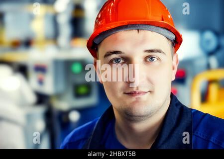 Portrait des jungen Ingenieurs im Helm in der Arbeitswelt in der Fabrik. Gasarbeiter blickt selbstbewusst direkt in die Kamera. Gasausrüstungsmonteur. Nahaufnahme des Mitarbeiters in Schutzkleidung im Heizraum. Heller Hintergrund. Stockfoto