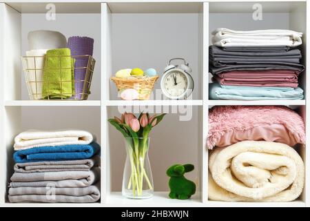 Stapel von Handtüchern Bettwäsche Bettdecken Kissen auf einem weißen Regal. Organisation der Lagerung. Osterfest Stockfoto