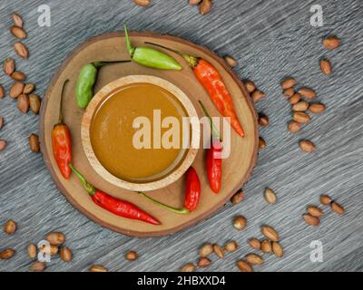 Erdnusssauce in einer kleinen Holzschüssel auf einem grauen Holztextur-Hintergrund. Stockfoto